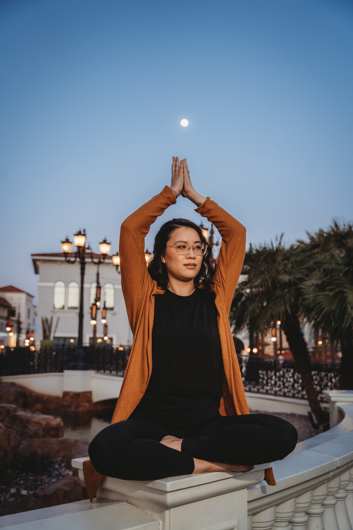 a wellness coach doing healing yoga in front of a building with the moon in the background.