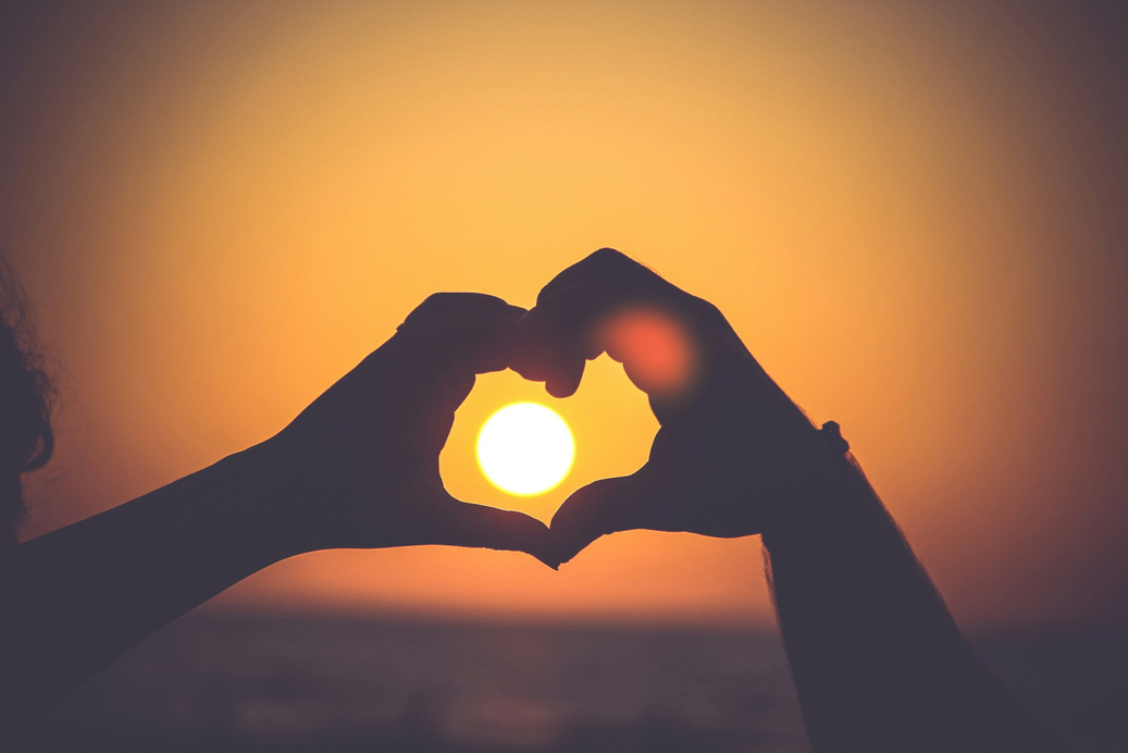 Couple making a heart with their hands against the sun